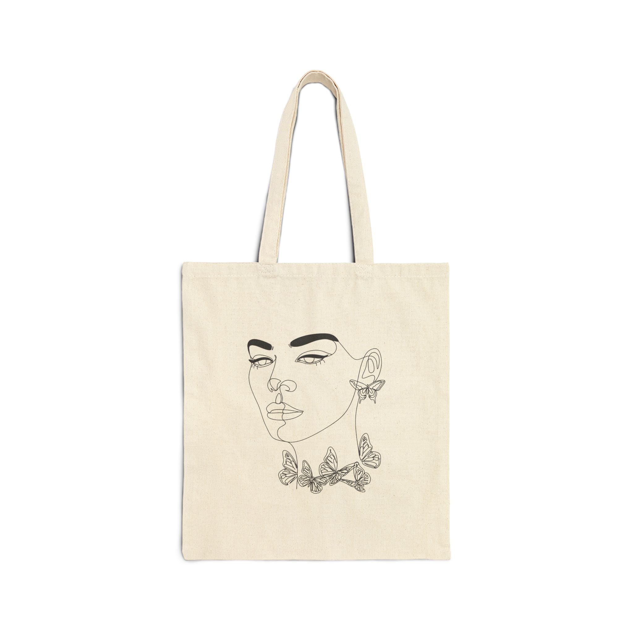 Beige tote bag with a black line art design of a face and butterflies on a white background